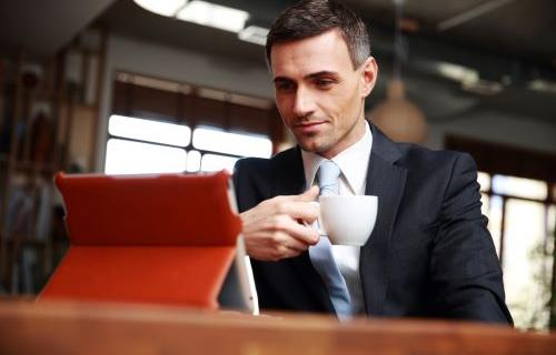 Businessman with a cup in his hand looking at iPad